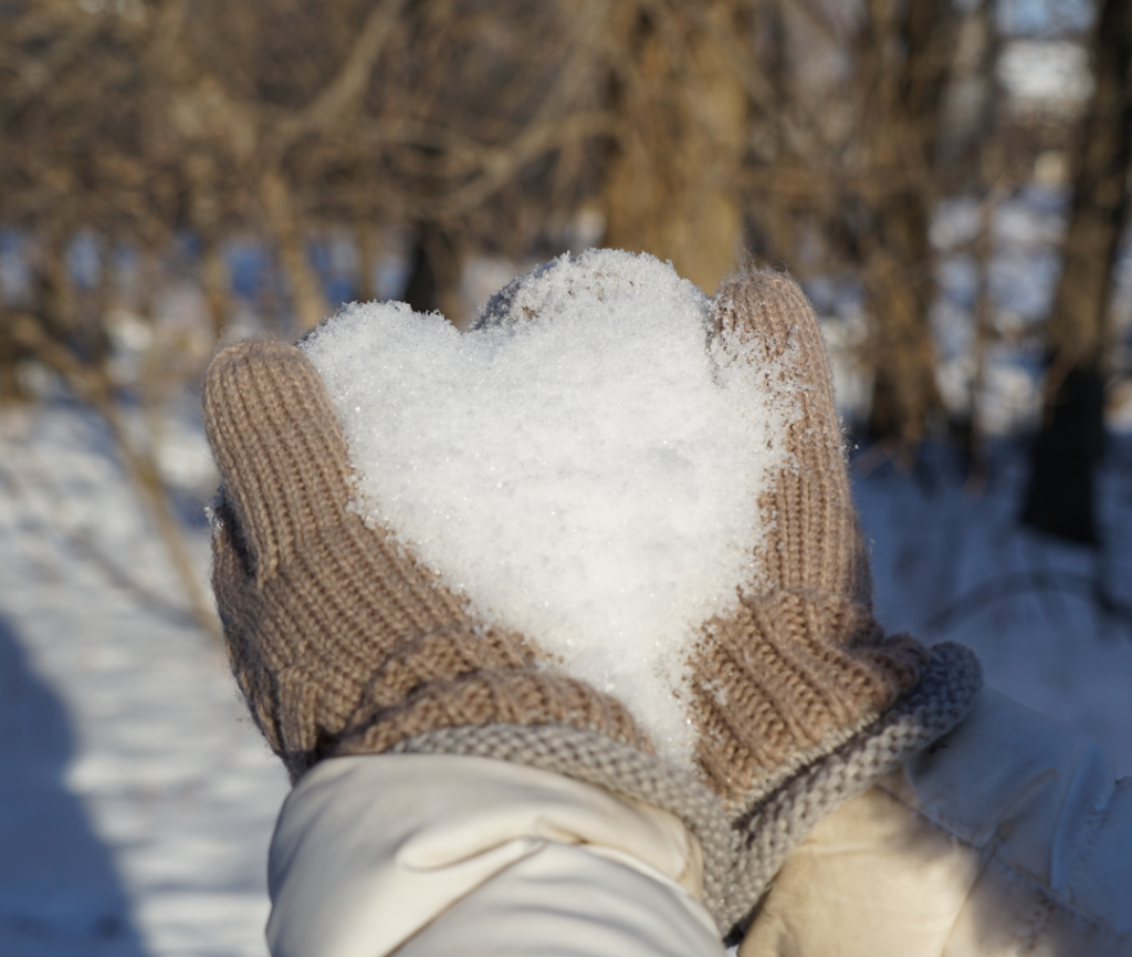 Mittens holding snow in the shape of a heart