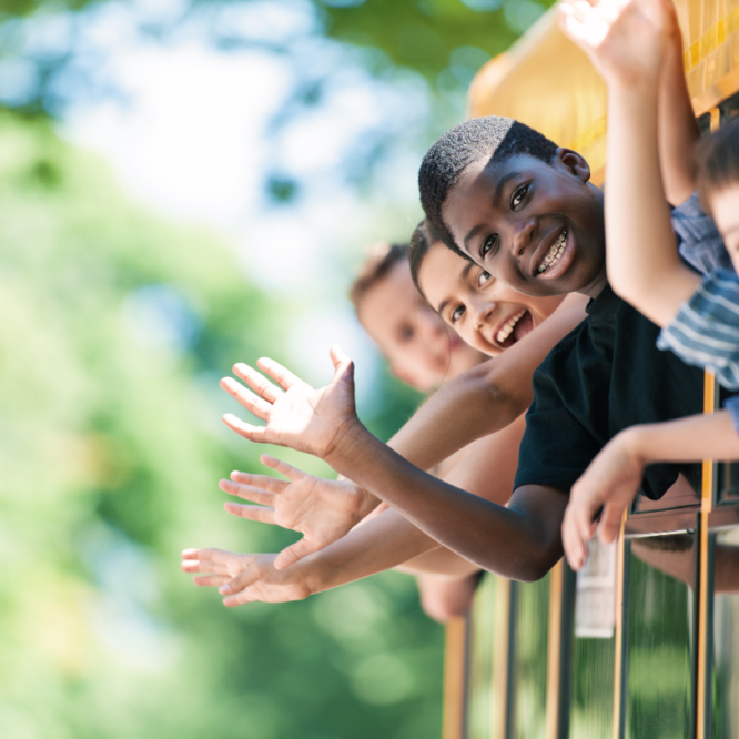 Kids leaning out of the school bus windows waving